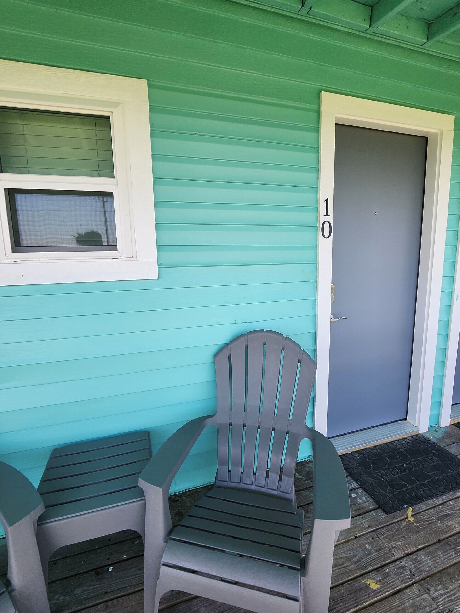 A teal-colored building with a door marked '10' and two plastic chairs outside.