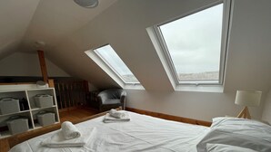 A bedroom with a sloped ceiling, skylights, a bed, a chair, a bedside table, and a lamp. - Talla Hope (Kilmuir)