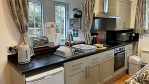 A compact kitchen with a dishwasher, a microwave, and a toaster. There is a window with curtains, a sink, and a first aid sign on the wall. - Talla Hope (Kilmuir)