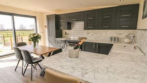 Una cocina moderna con armarios oscuros, encimera de mármol y comedor con mesa y sillas.