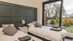 Un dormitorio con dos camas, una mesita de noche con lámpara y vistas al exterior a través de un amplio ventanal.