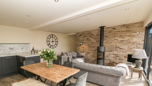 Una sala de estar moderna con chimenea, un comedor con mesa y sillas de madera, y una cocina con armarios oscuros y encimera de mármol.