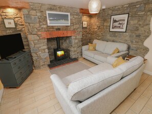 Una sala de estar con pared de piedra, chimenea, sofá gris y televisor sobre un mueble.