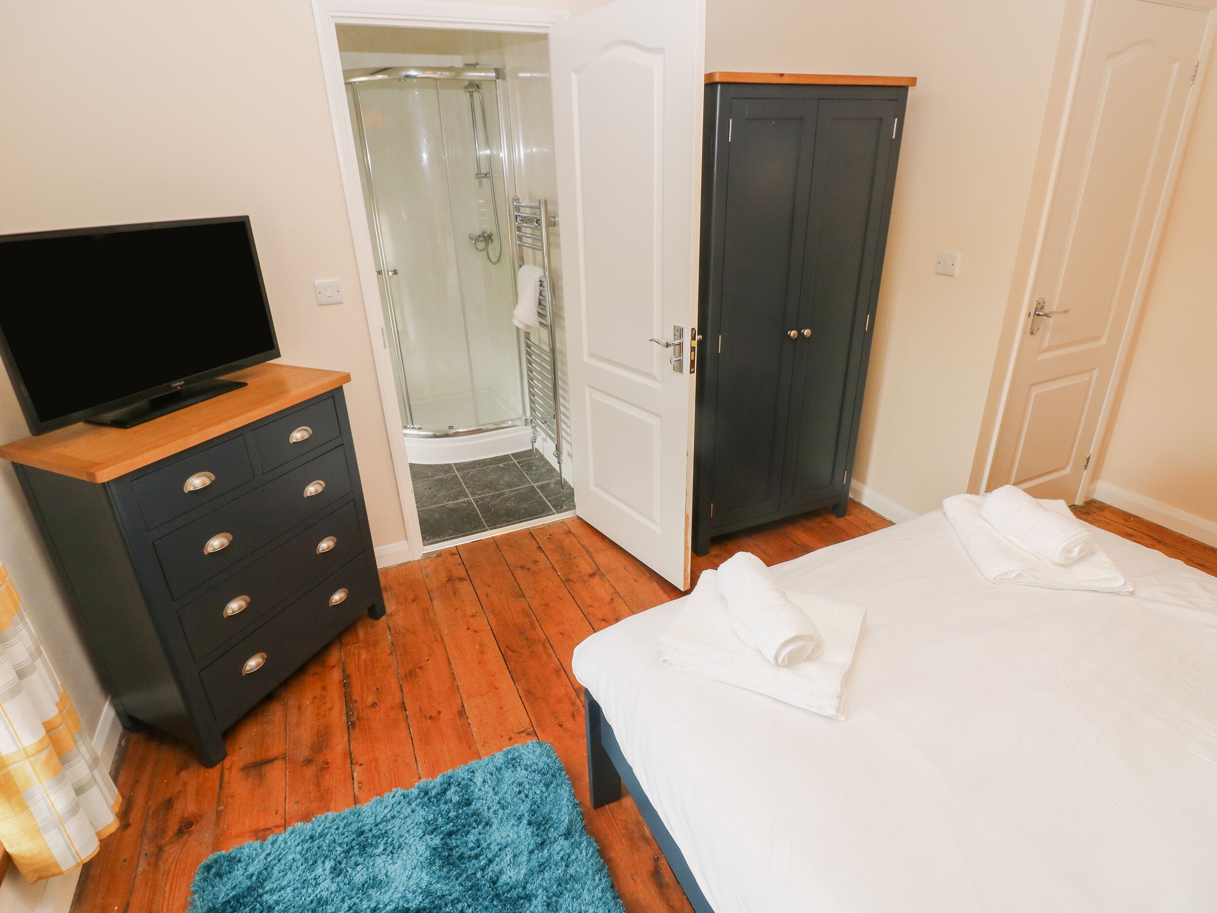 A bedroom with a bed, a TV on a dresser, a shower, and a wardrobe.