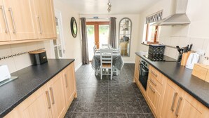 A kitchen with wooden cabinets, a black countertop, and a tiled floor. - Brynawel (Carmarthen)