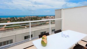 A balcony with a white table, two coconuts, and a view of the sea and cityscape. - Excelente casa em Porto das Dunas (Aquiraz)