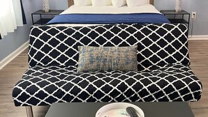 Ein Schlafzimmer mit einem Bett, einem schwarz-weißen Sofa mit Muster, einem kleinen Tisch mit Fernbedienung und dekorativen Wandverkleidungen.
