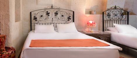 A double bed with white linens and an orange throw, a nightstand with a lamp, and a red floral-patterned rug.