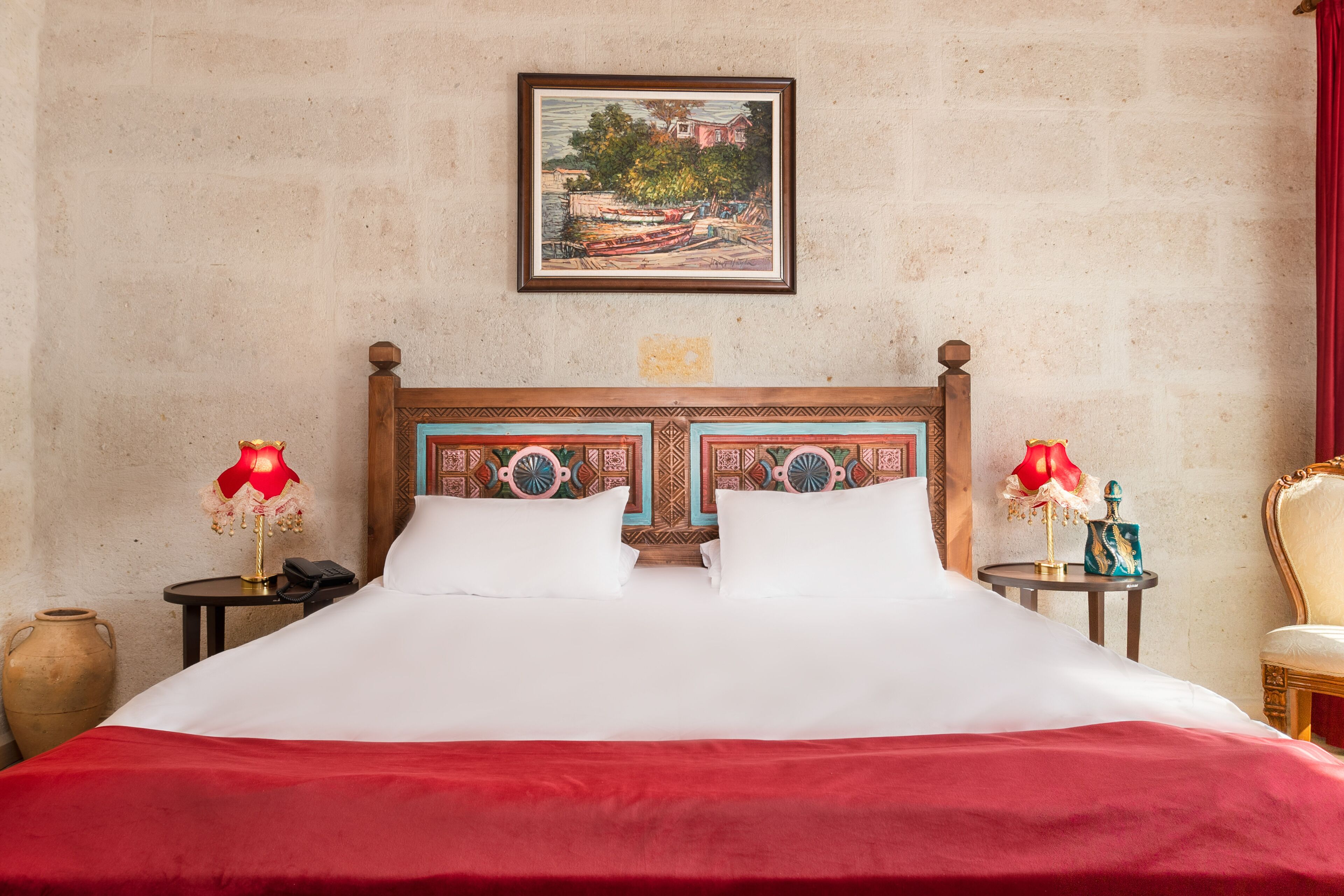 A neatly made bed with white linens, a wooden headboard with intricate designs, and two bedside tables with red lamps.