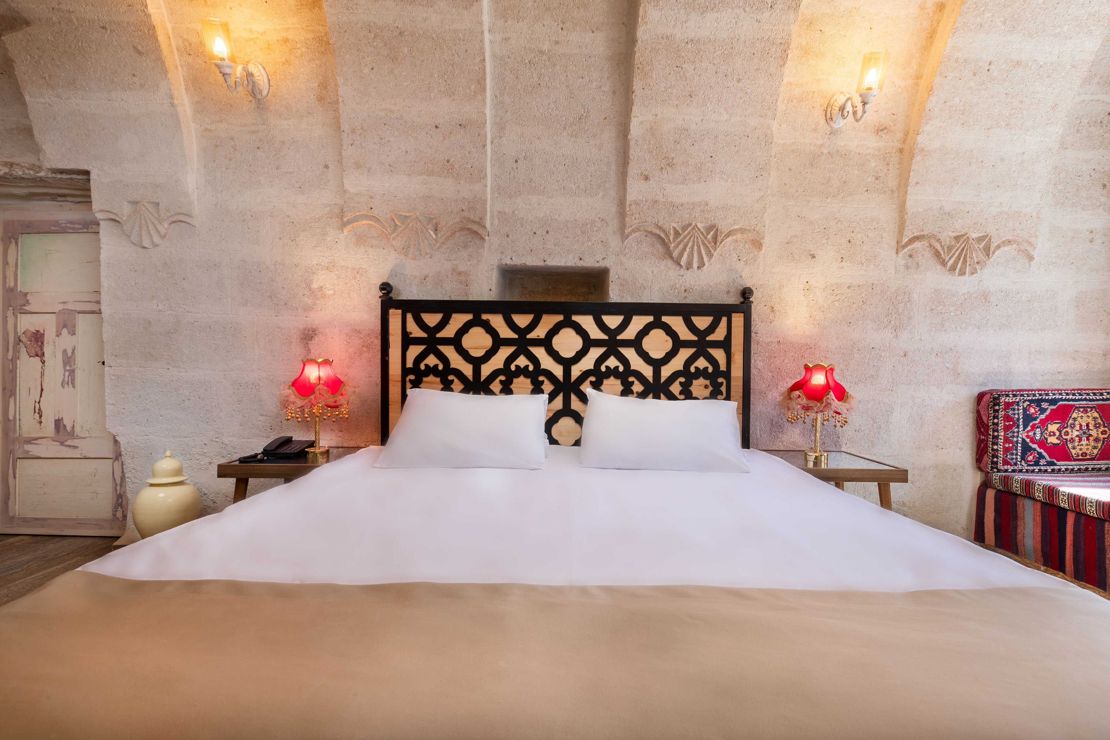 A bed with a black headboard, two bedside lamps, a nightstand, and a decorative wall.