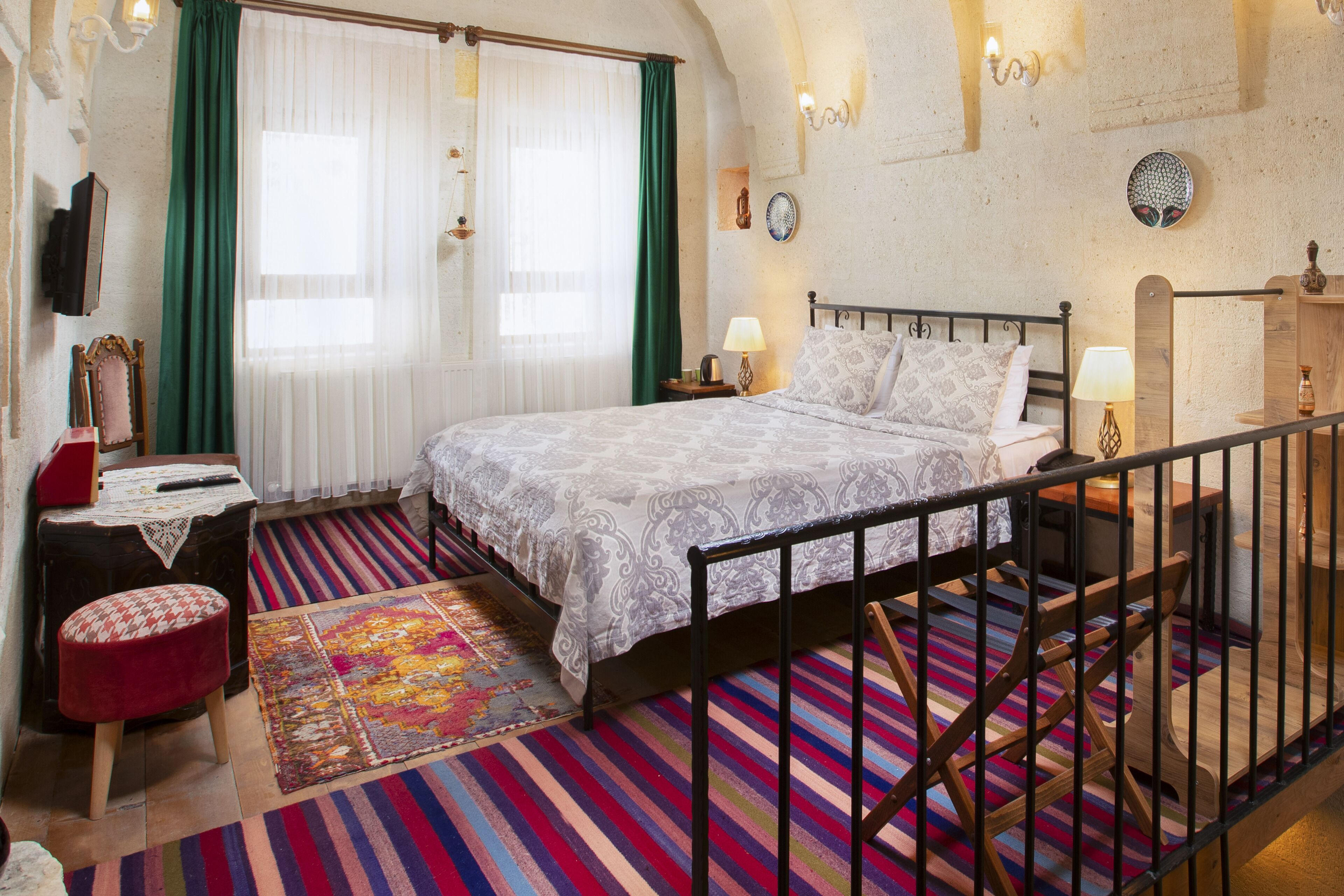 A bedroom with a bed, a nightstand, a lamp, a dresser, a mirror, and a window with curtains.