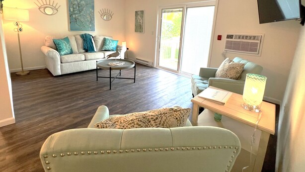 Ein Wohnzimmer mit Sofa, Sessel, Couchtisch und einem an der Wand befestigten Fernseher.