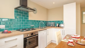 A compact kitchen with teal backsplash, a stove, oven, and a sink. - Roundham Cottage (Bridport)
