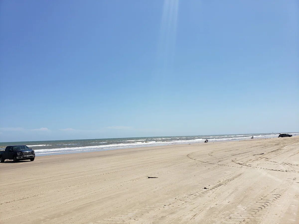 A beach with a truck parked on the sand, a clear sky, and the ocean in the background.