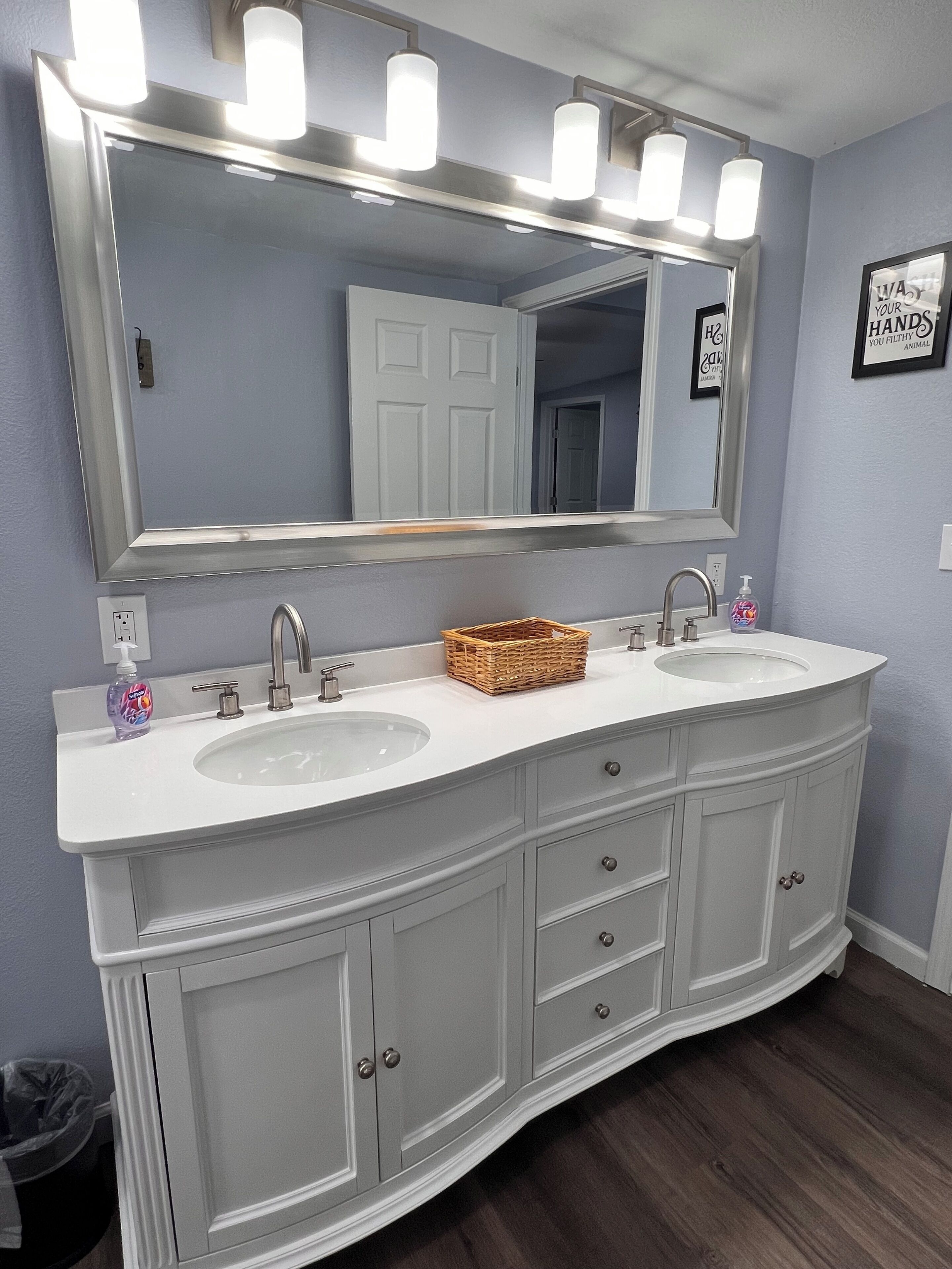 A bathroom with a double sink vanity, a large mirror, and a basket on the countertop.