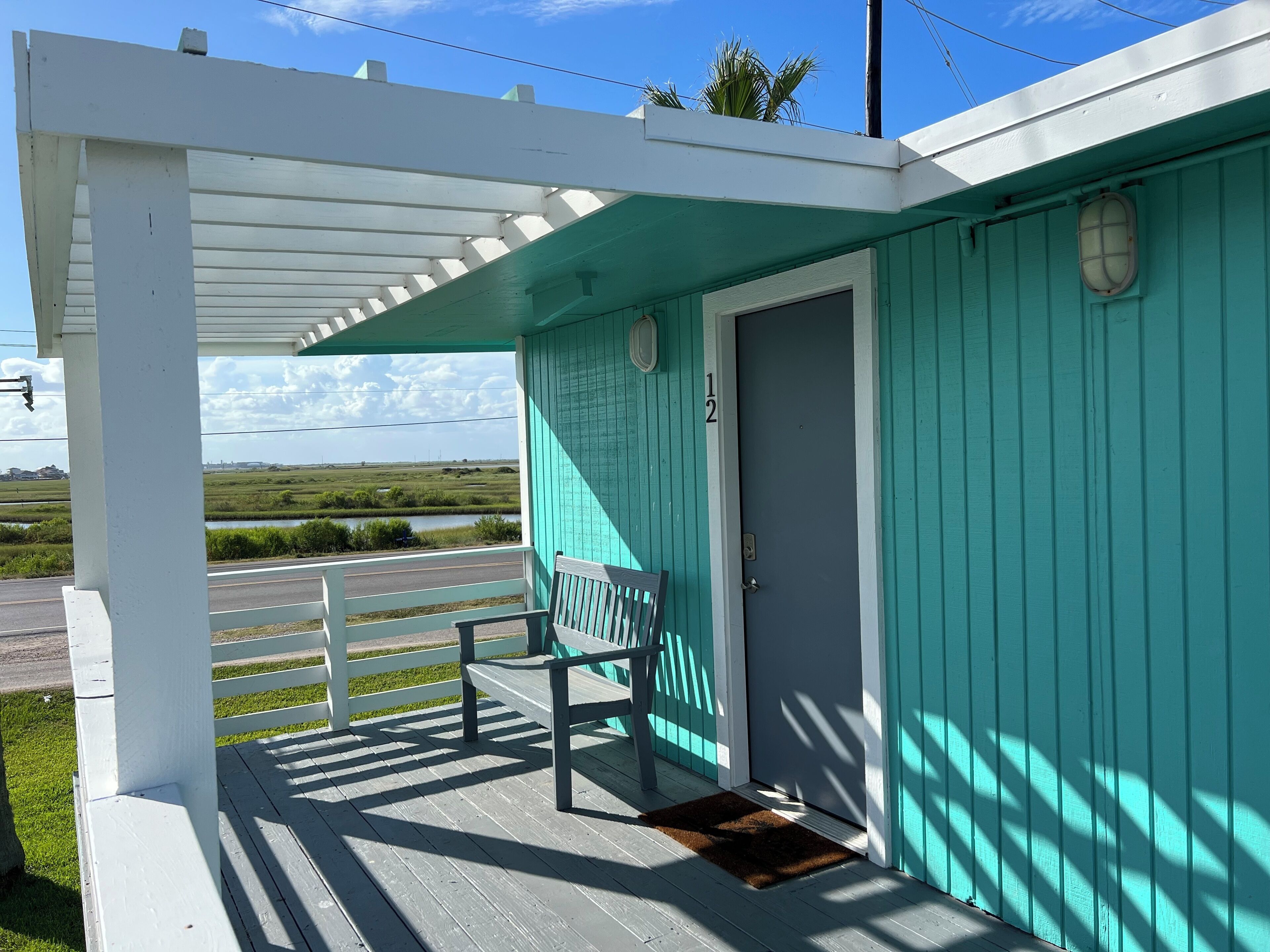 A turquoise building with a porch, a bench, and a door marked "12".