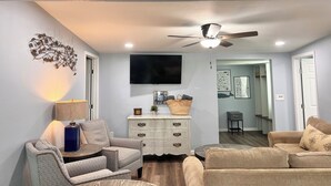 Una sala de estar con ventilador de techo, televisor y un cartel en la pared que dice "Life is Better At the Beach".