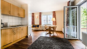 A modern kitchen with wooden cabinets, a dining area with a table and chairs, and a large window with curtains. - Bikehotel Freiburg (Merzhausen)