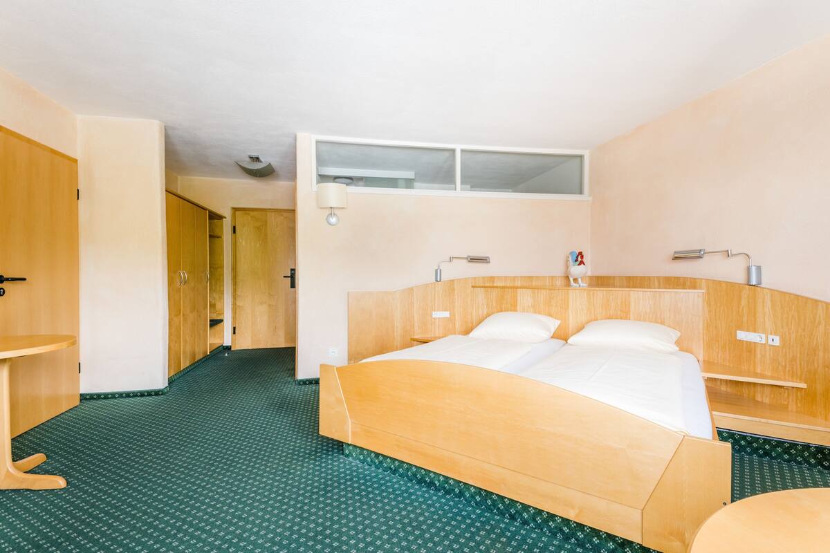 Habitación de hotel con una cama de madera, una mesita pequeña, un espejo y un piso con estampado verde.