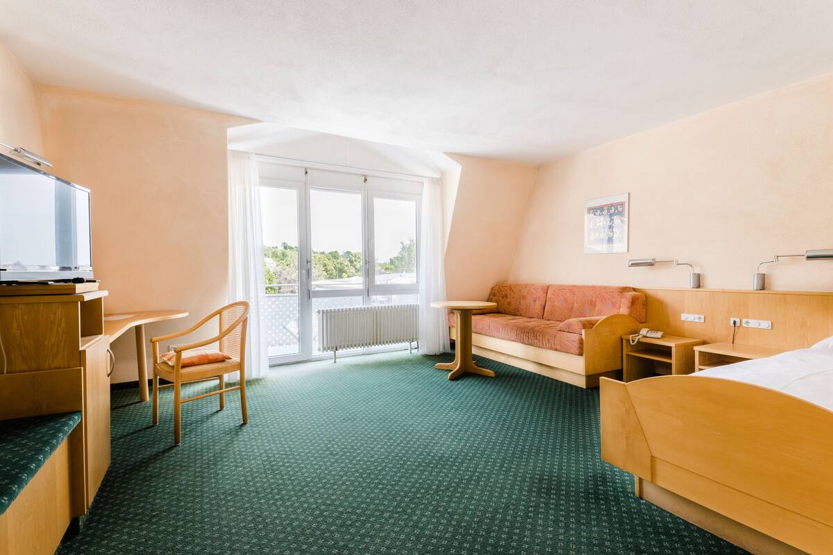 Habitación de hotel con cama, escritorio, silla, sofá, mesita y televisor.