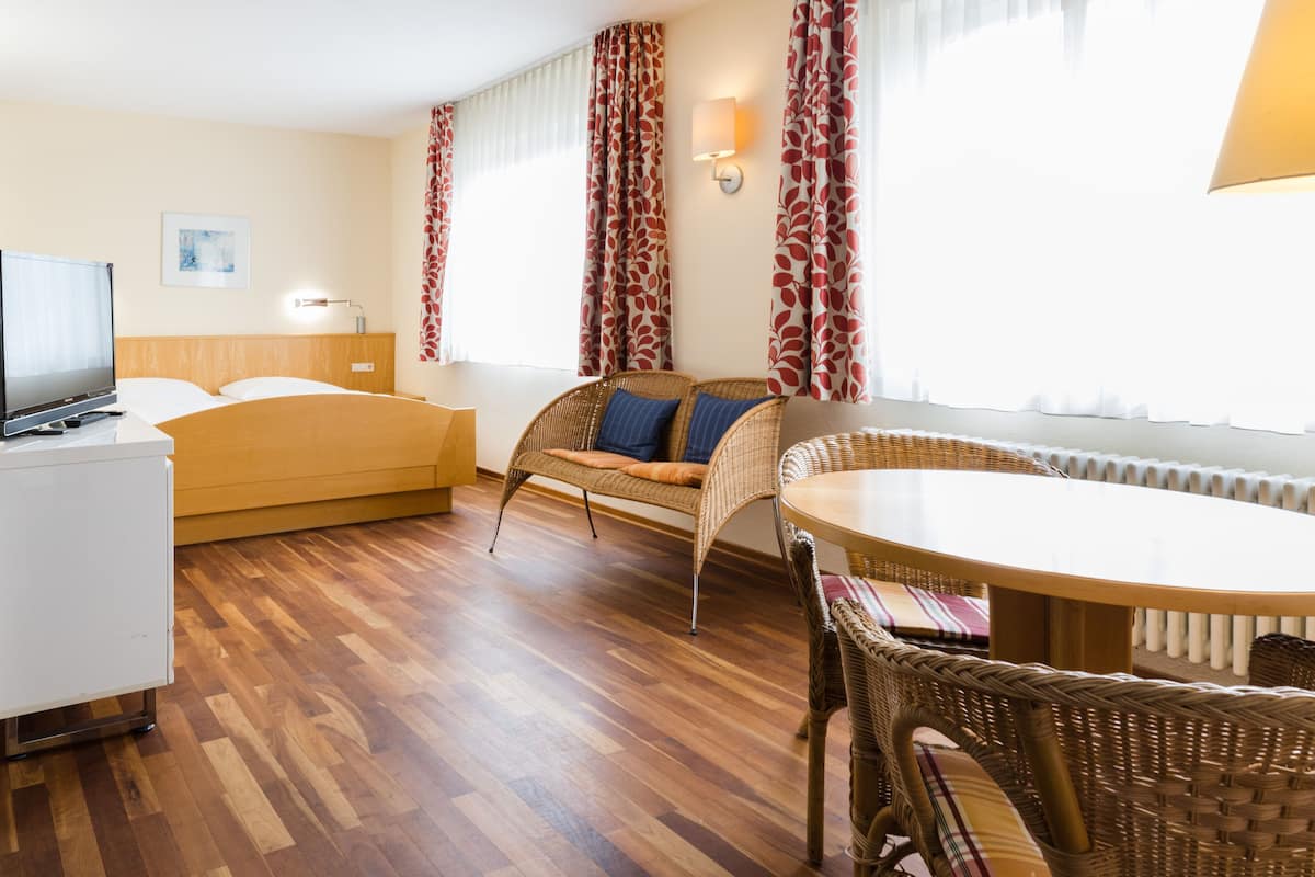 Habitación de hotel con cama, televisor, mesa de comedor, mobiliario de mimbre y radiador.