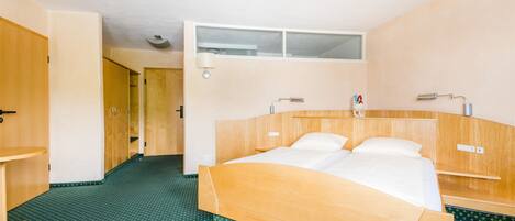 Una habitación de hotel con una cama de madera, una mesita pequeña y un suelo con estampado verde.