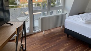 A bedroom with a large window, a bed, a desk, and a radiator. - Bikehotel Freiburg (Merzhausen)