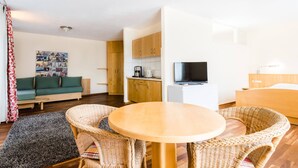 A modern living room with a sofa, a dining table with chairs, a kitchen area, and a television. - Bikehotel Freiburg (Merzhausen)