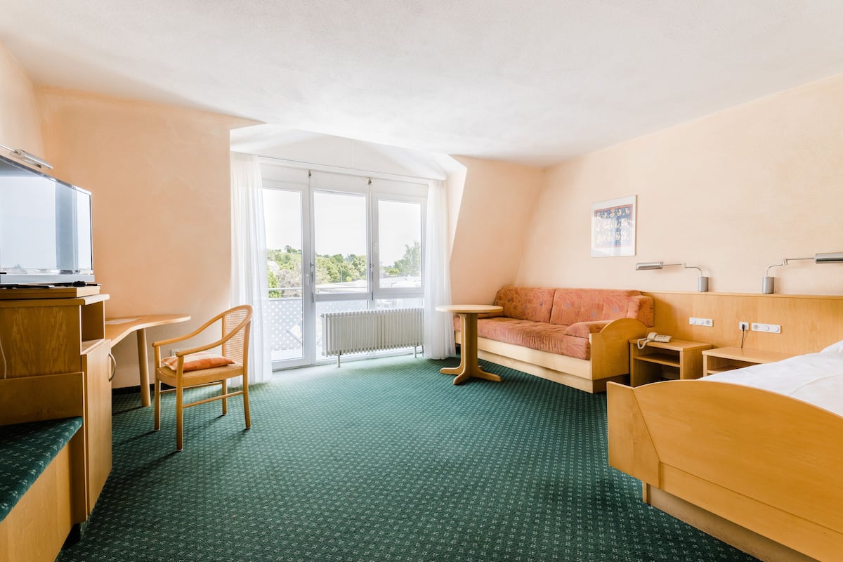 Una habitación de hotel con cama, escritorio, silla, sofá, una mesita y televisión.