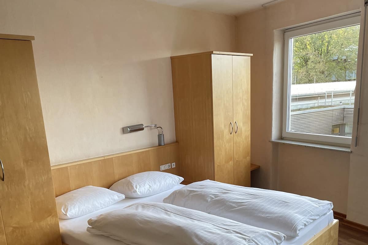 Un dormitorio con una cama de madera, un armario, una mesita de noche y una ventana con vistas a árboles.