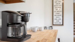 Una cuina moderna amb una cafetera negra i elegant, un taulell de fusta i una llista emmarcada de ciutats a la paret.
