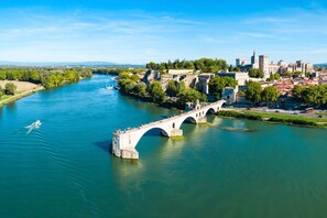 Spanning a serene river, this historic bridge connects two city parts, surrounded by lush greenery and a majestic castle in the background.