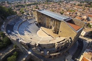 Situated in a densely built urban area, this ancient amphitheater features a partially restored stage area and a modern bridge connecting to surrounding buildings.