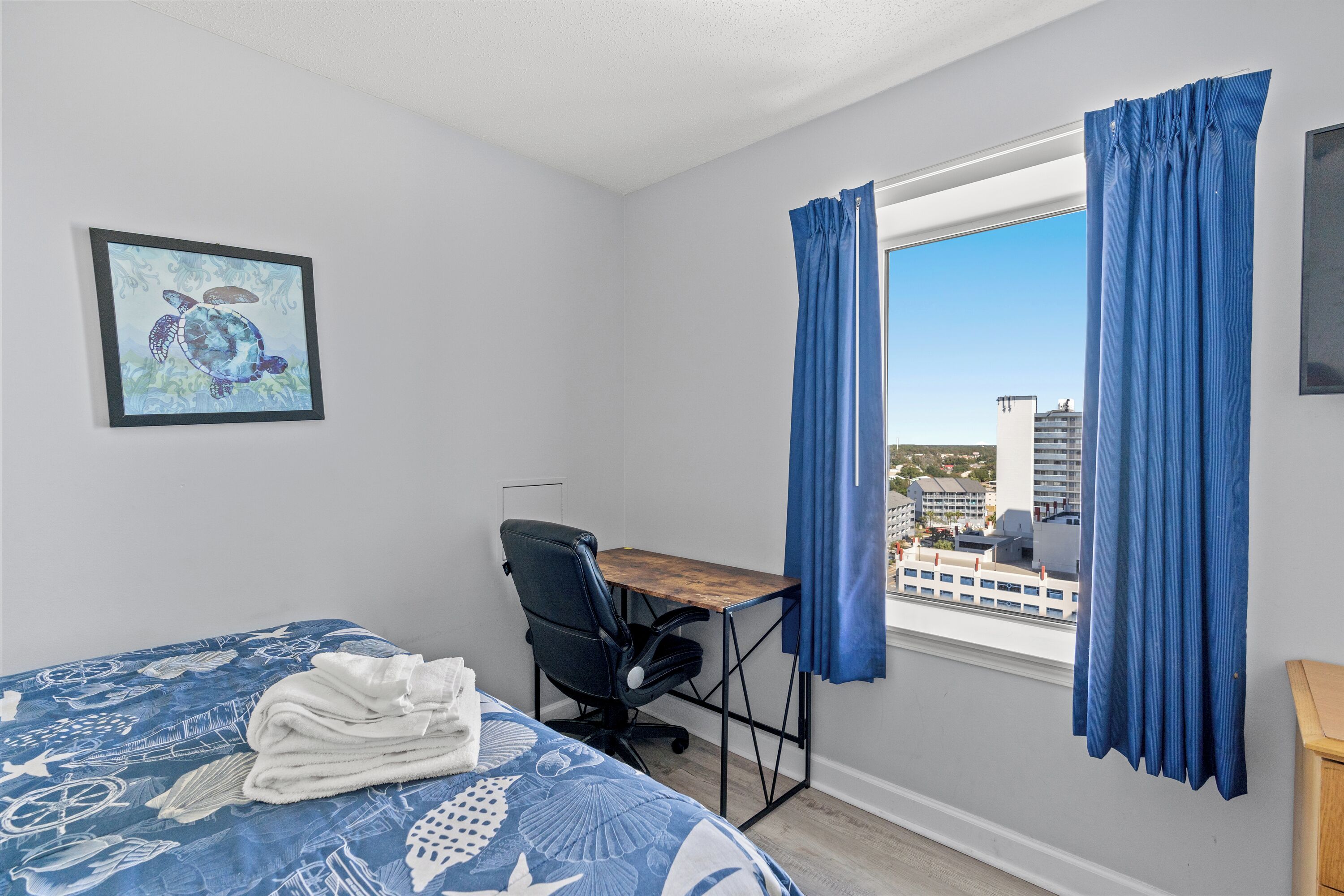 Una habitación con cama, escritorio, silla y ventana con cortinas.