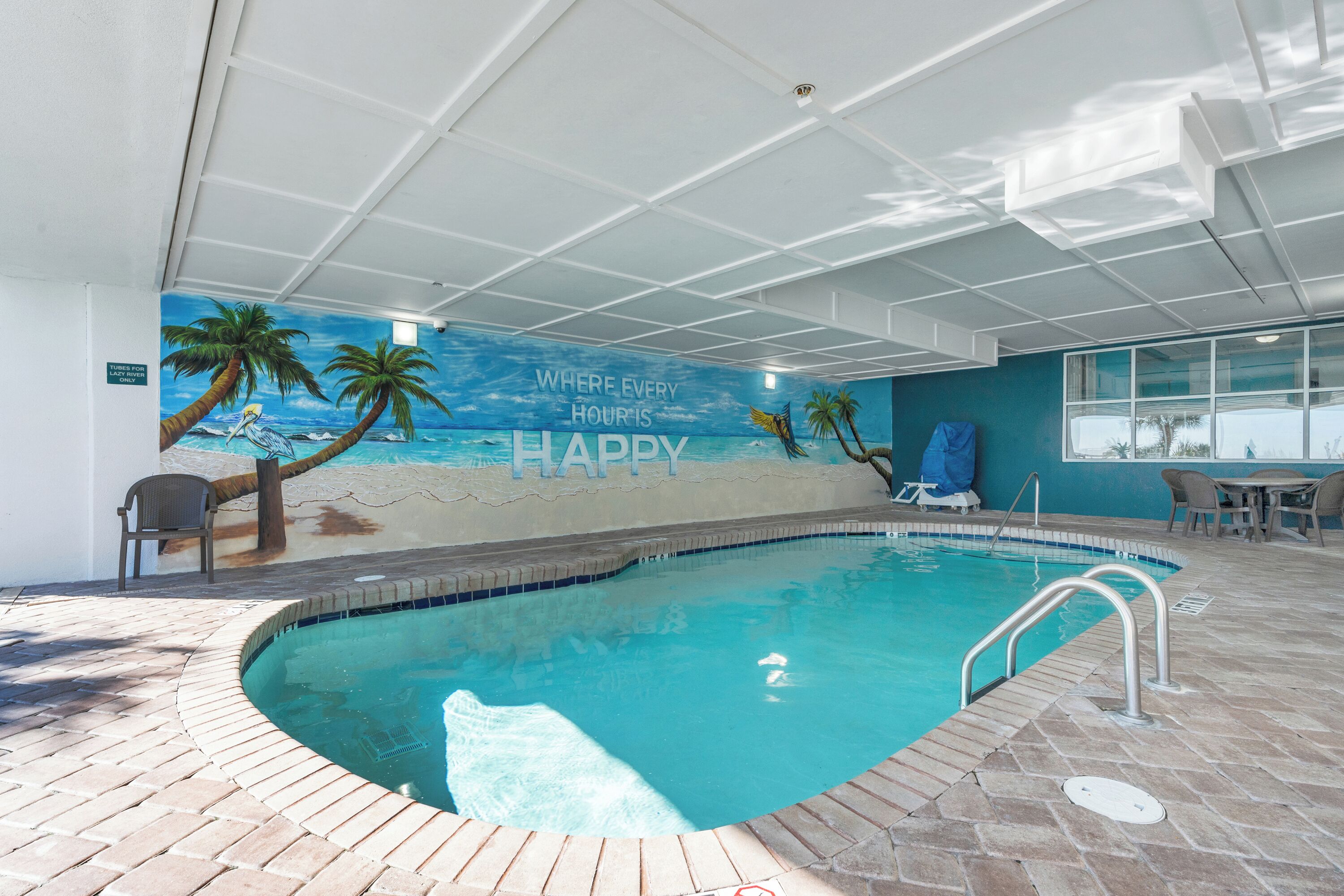 An indoor swimming pool with a mural of a beach scene and the text "Where every hour is happy."