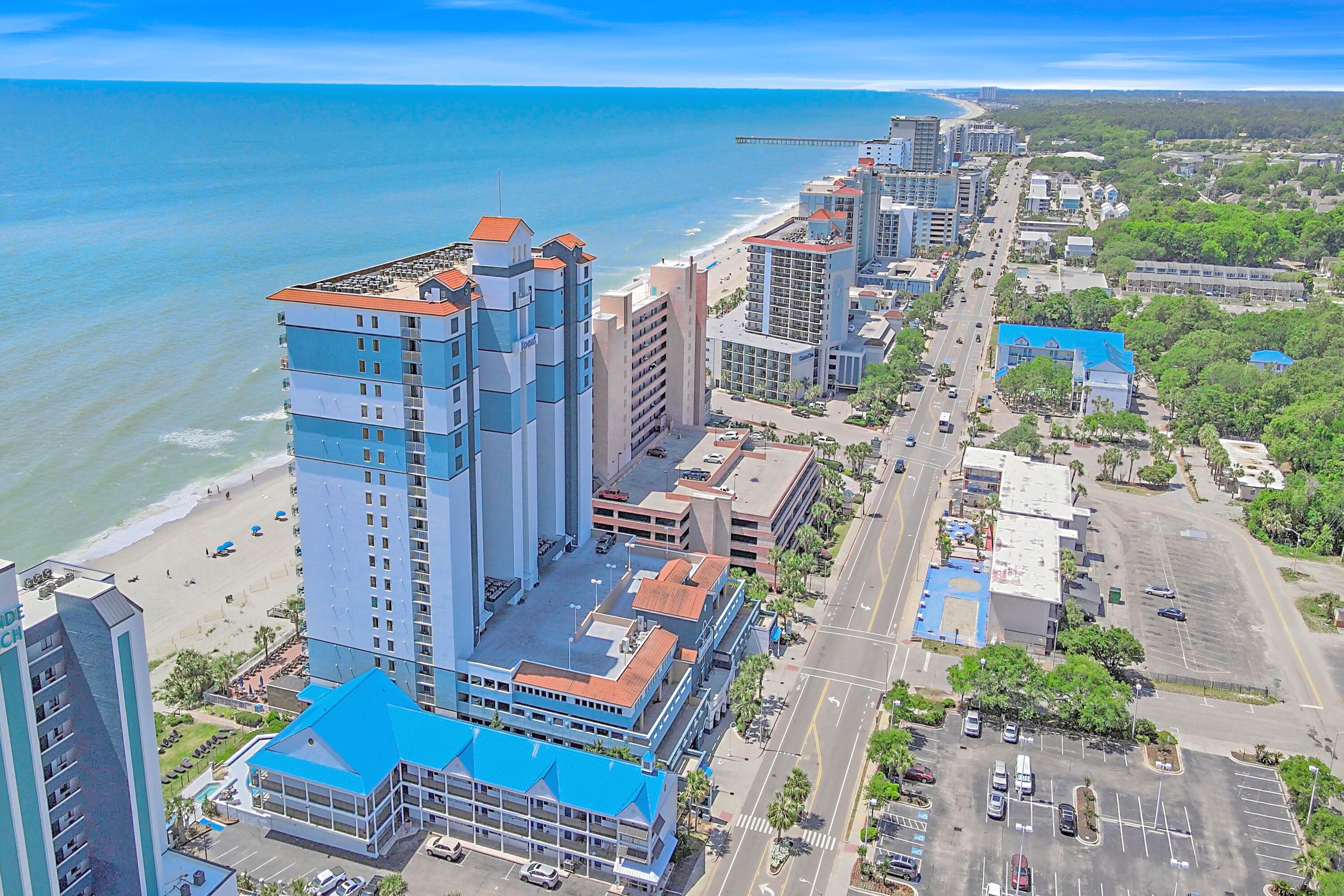 A coastal cityscape with high-rise buildings, a beach, and a parking lot.