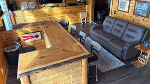 Ein gemütliches Blockhaussinnenzimmer mit einer Holzeinrichtung, einem grauen Sofa und einem an der Wand befestigten Fernseher.