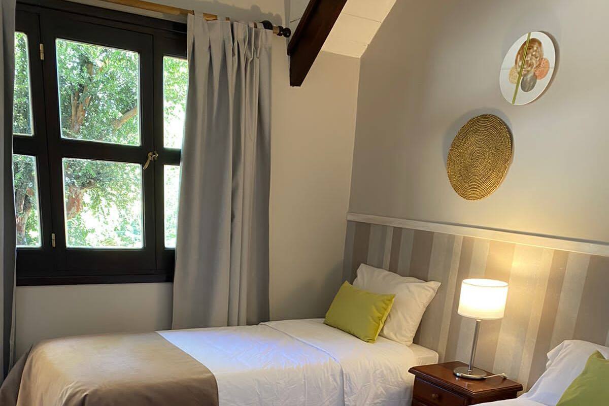 Une chambre avec deux lits, une fenêtre avec des rideaux, une lampe de chevet et un tableau accroché au mur.