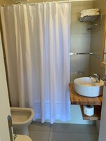 Un baño con inodoro, bidé, cortina de ducha blanca y un lavabo con encimera de madera.