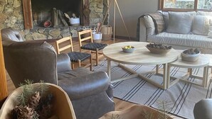 A cozy living room with a fireplace, wooden beams, a sofa, and a dining table.