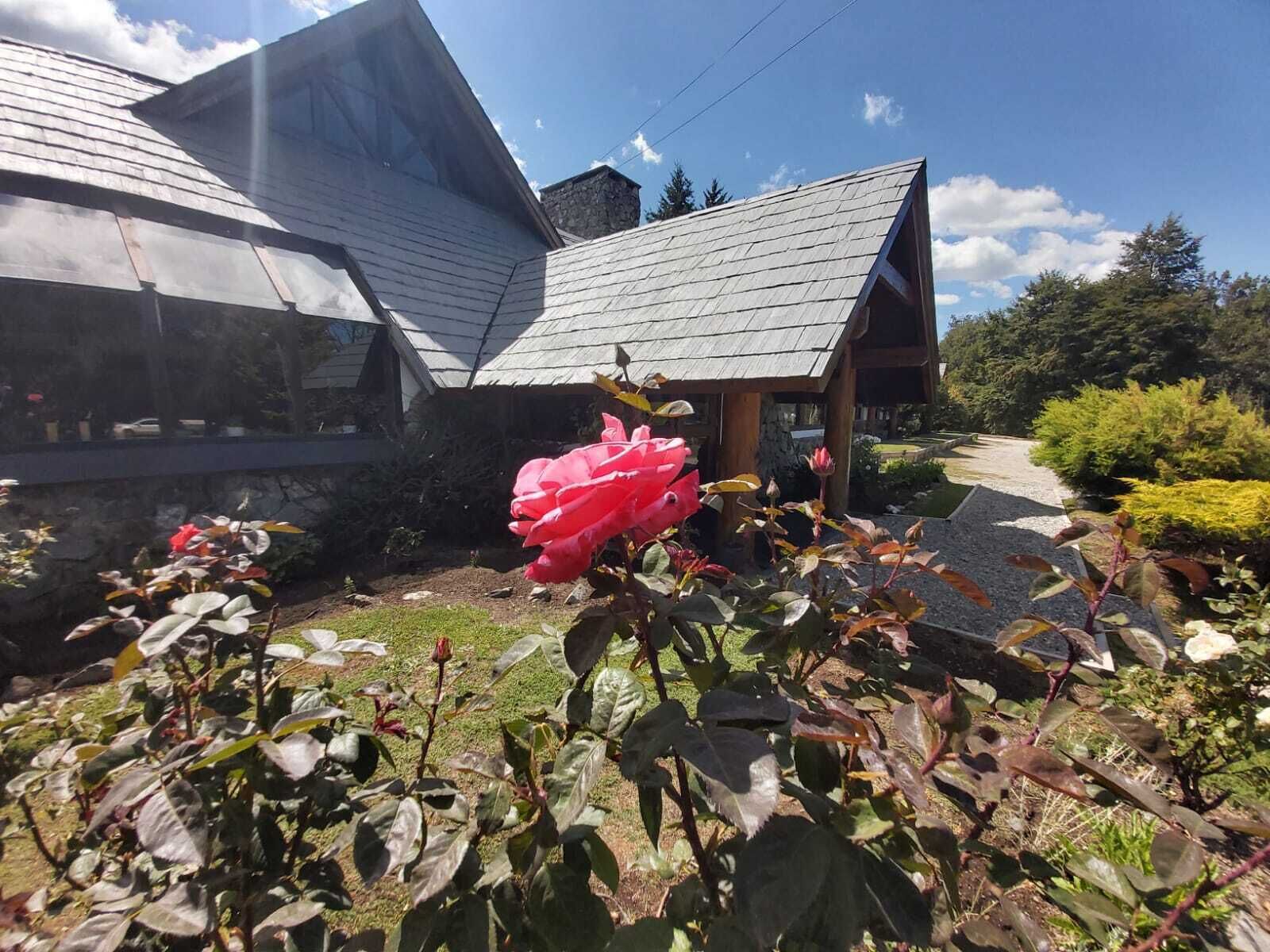 A house with a sloped roof, a garden with roses, and a stone wall.
