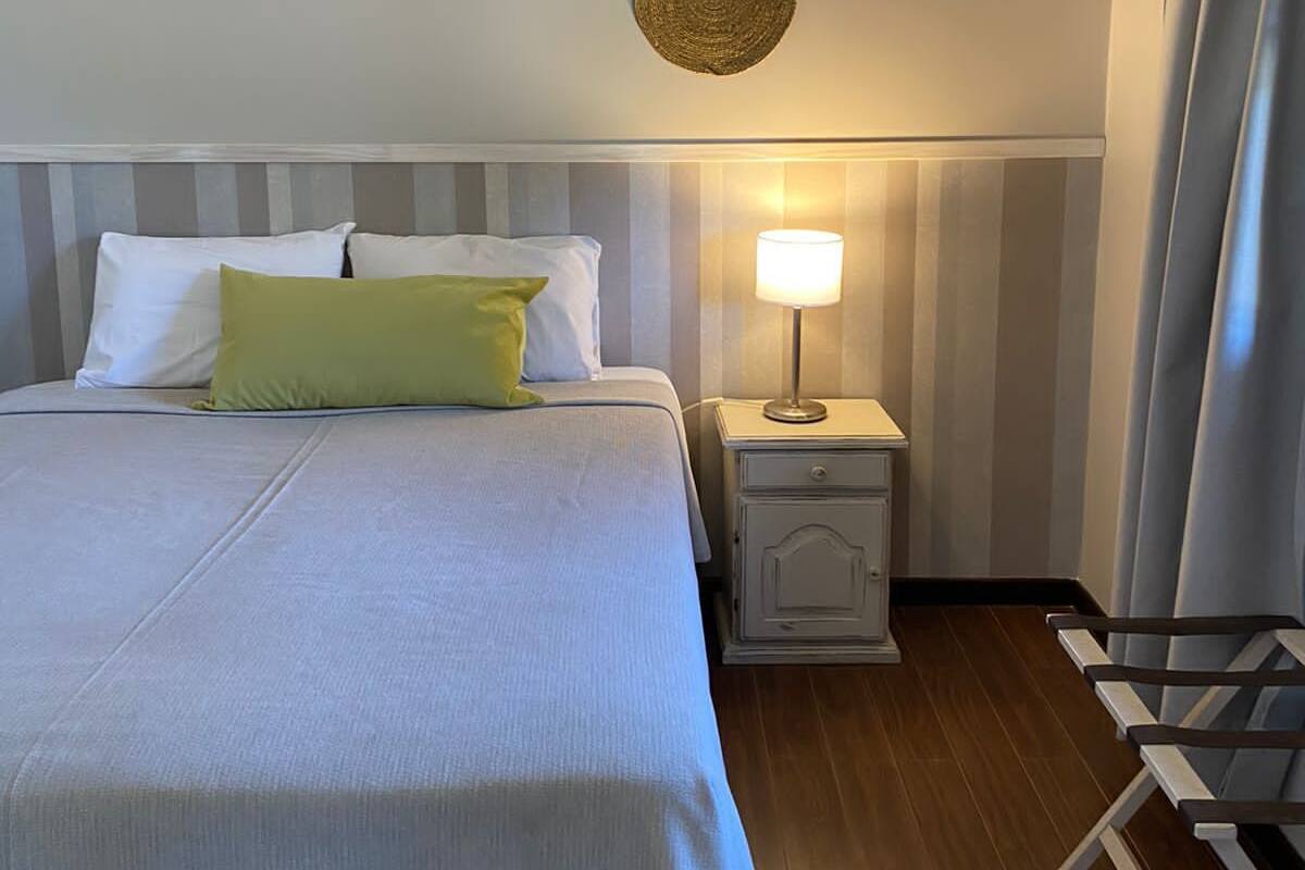 Un lit bien fait, avec des oreillers blancs et verts, une table de chevet avec une lampe et un plancher en bois.