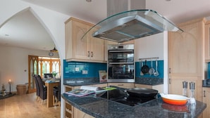 A modern kitchen with a curved glass island, wooden cabinets, and a built-in oven. - Fairholme (Port Isaac)