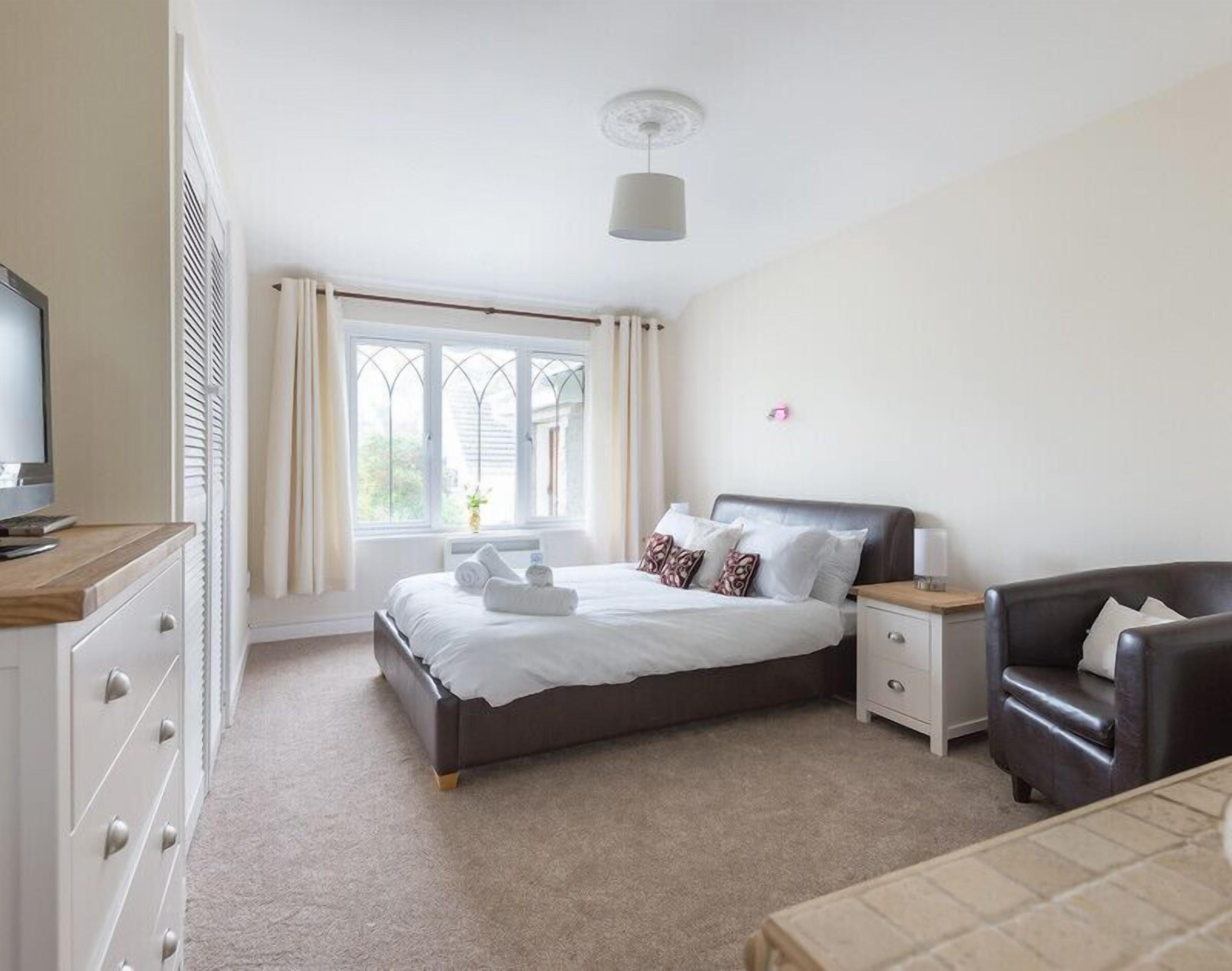 A bedroom with a bed, bedside tables, a chair, a television, and a window with curtains.