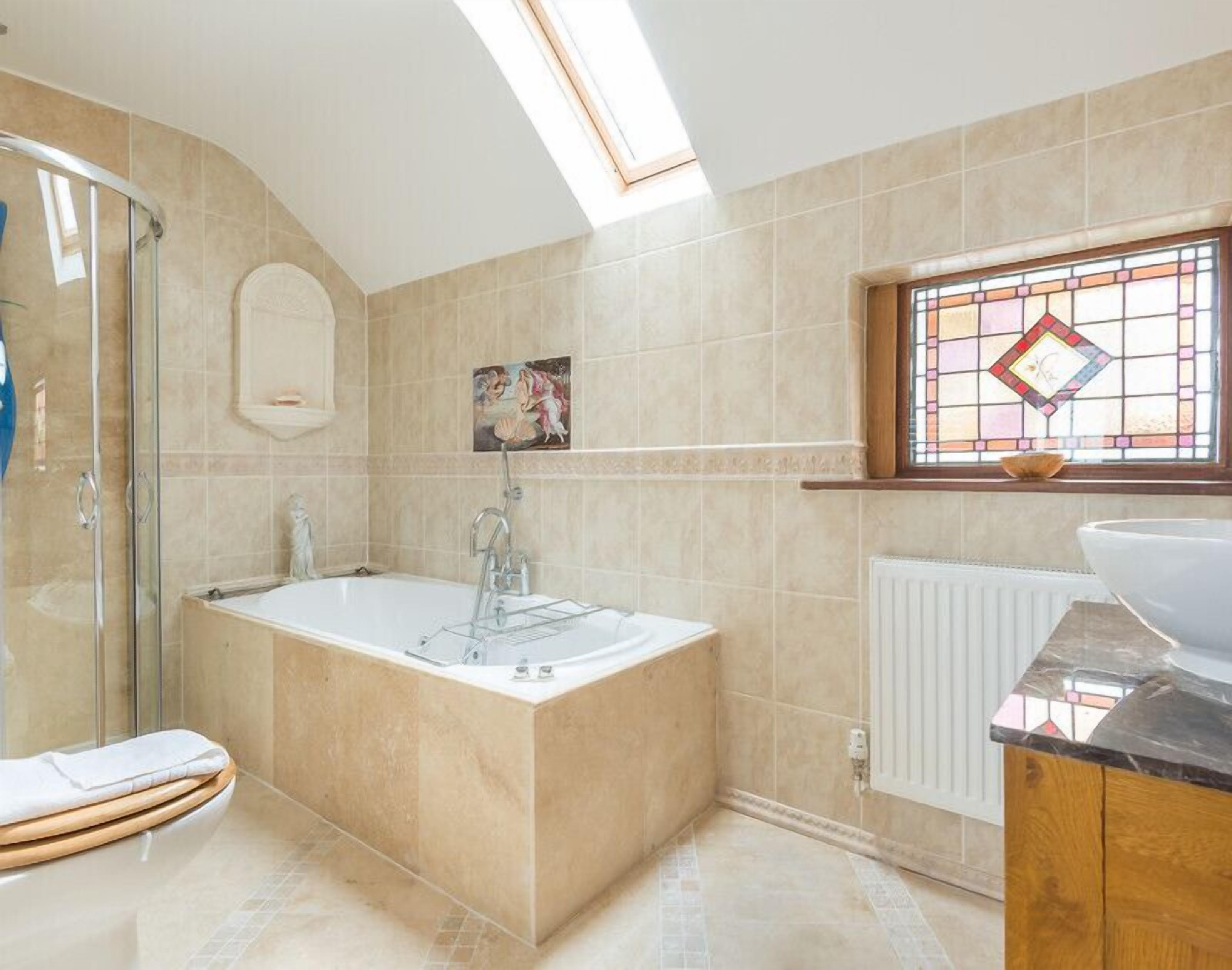 A modern bathroom with a freestanding bathtub, a glass shower enclosure, and a window with stained glass.