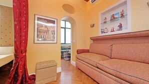 Una sala de estar con un sofá, una mesita, un cuadro enmarco y una estantería con figuritas.