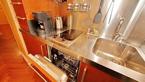 Una cocina compacta con lavavajillas, cafetera, hervidor y lavabo.