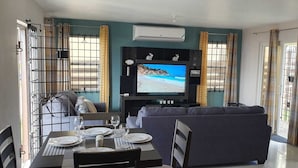 A living room with a TV, sofa, dining table, and chairs.