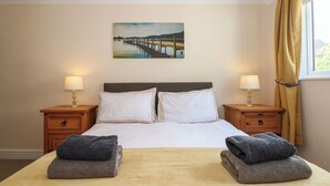 A hotel room with a bed, two nightstands, a painting on the wall, and a window with curtains. - Inglewood (Keswick)