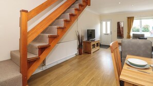 A staircase with wooden steps and a carpeted landing, a television on a wooden stand, a dining table with a plate and a spoon, and a window with curtains. - Inglewood (Keswick)